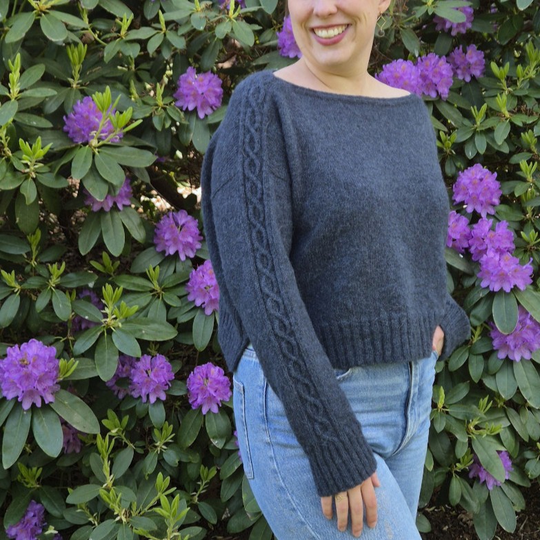 A boxy, dropshoulder sweater with an elegant boat neck and a delicate cable detail.